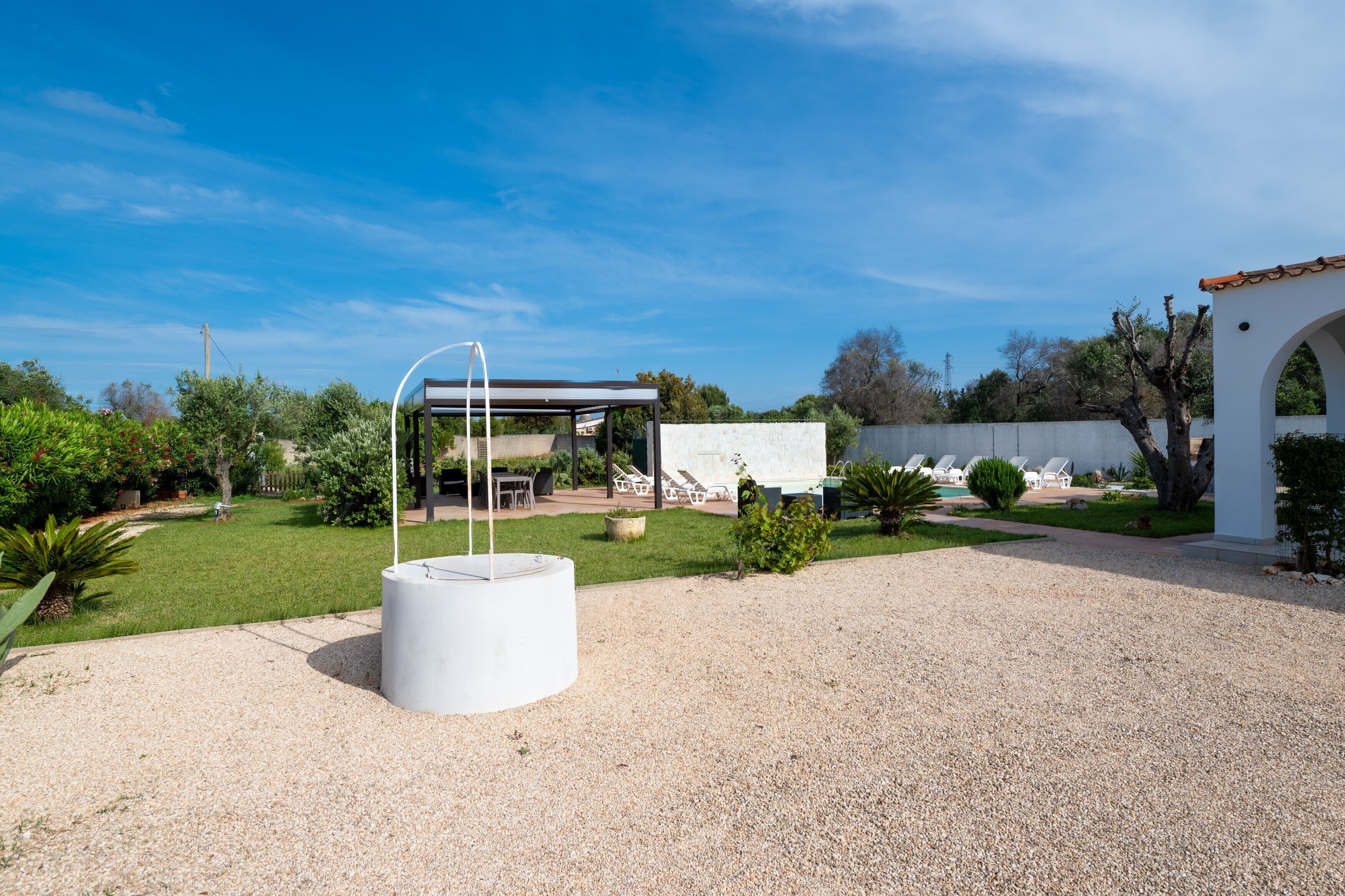 Un'area esterna moderna con una struttura bianca, una zona relax coperta e una piscina.