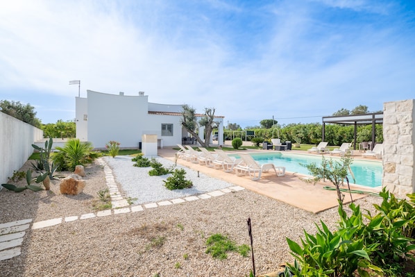 A modern outdoor pool area with lounge chairs, a stone wall, and a white building.