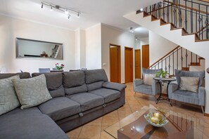 A living room with a sofa, armchairs, a coffee table, and a staircase.