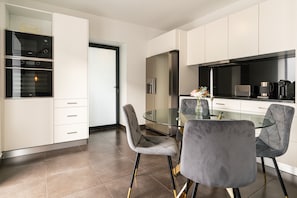 A modern kitchen with built-in appliances, a glass dining table, and grey upholstered chairs. - Holiday Home 'Melblue' with Sea View, Private Terrace and Wi-Fi (Calheta)