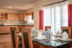 Een eethoek met een glazen tafel voor zes personen, houten stoelen en uitzicht op de keuken op de achtergrond.