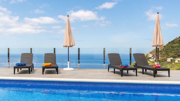 A poolside area with lounge chairs and umbrellas, overlooking a clear blue sky and a distant coastline.