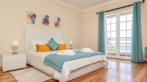 A bedroom with a bed, nightstands, a white rug, a window with curtains, and artwork on the wall.