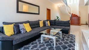 A modern living room with a sectional sofa, glass coffee table, and a staircase leading to another level.