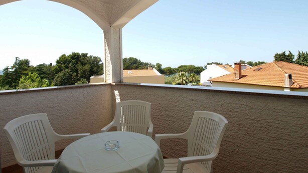 A balcony with a table and two chairs, overlooking a residential area with houses and trees.