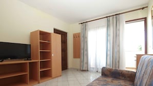 A living room with a TV, wooden shelving, a sofa, and a door.