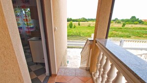 A balcony with a view of a green field, a tiled floor, and a chair.
