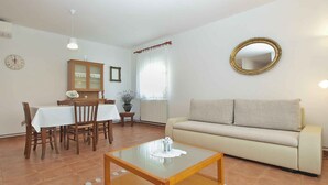 Un saló amb un sofà, una taula de centre, una taula de menjador amb cadires, un armari, un mirall i un rellotge penjat a la paret.