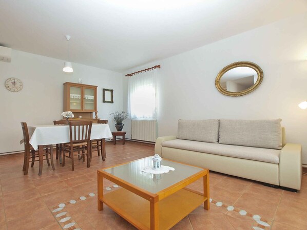 Un salon comprenant un canapé, une table basse, une table à manger avec des chaises, un meuble, un miroir et une horloge murale.