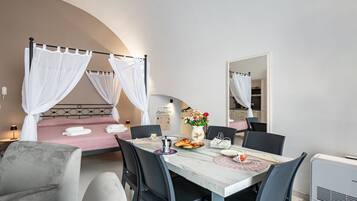 Ein Schlafzimmer mit einem Himmelbett, einem Essbereich mit Tisch und Stühlen sowie einer kleinen Küche im Hintergrund.