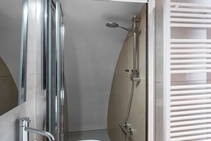 A modern bathroom with a glass shower enclosure, a handheld showerhead, and a toilet.