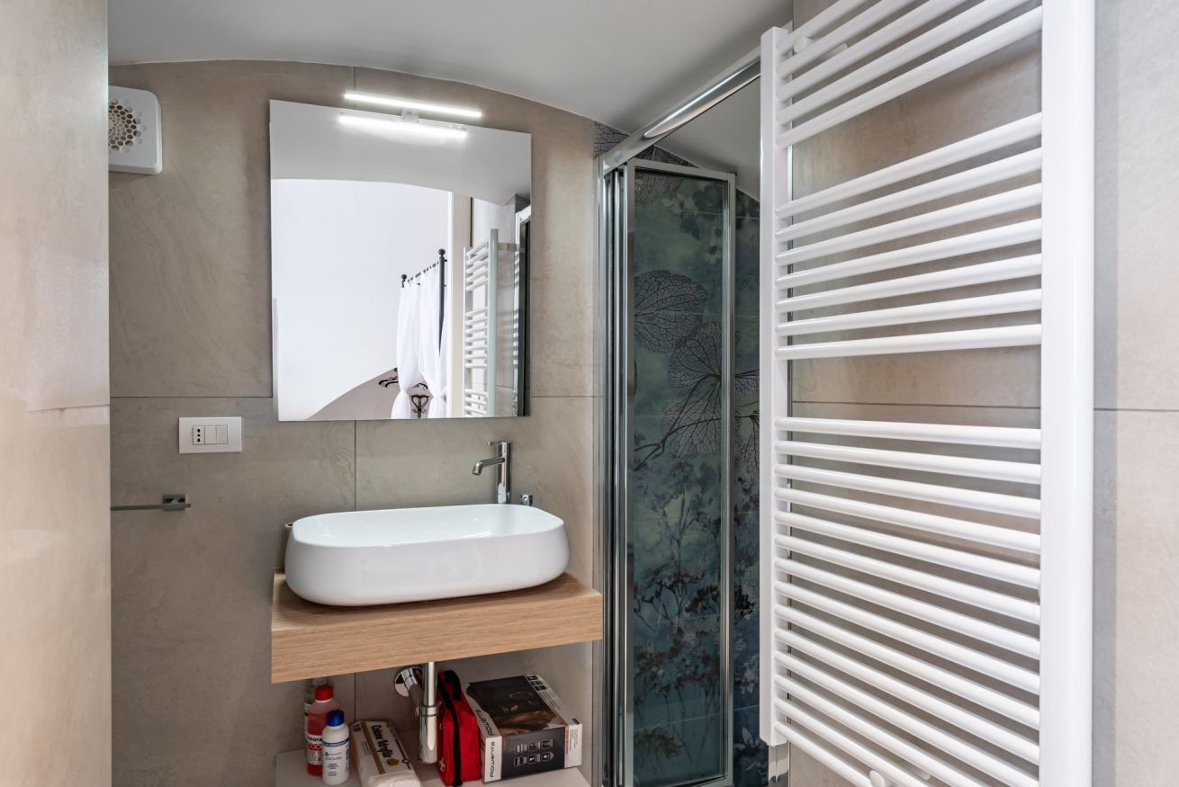 Une salle de bain avec un lavabo blanc, un miroir et une douche avec des stores blancs.