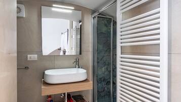 Une salle de bain avec un lavabo blanc, un miroir et une douche avec des stores blancs.