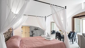 Een slaapkamer met een bed, witte gordijnen, een eethoek en een spiegel.