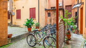 A narrow alley with bicycles parked along the side, potted plants, and buildings with red shutters. - GuestHost - Functional and modern studio apartment of approximately 17 sqm located on the ground floor of a renovated period building WITHOUT a lift (one step to access it). The apartment is located in a quiet, traffic-free street, just a 7-minute walk f (Padova)