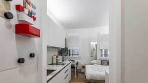 A compact hotel room with a kitchenette, a bed, a desk, and a window. - GuestHost - Functional and modern studio apartment of approximately 17 sqm located on the ground floor of a renovated period building WITHOUT a lift (one step to access it). The apartment is located in a quiet, traffic-free street, just a 7-minute walk f (Padova)