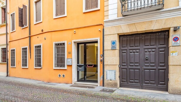 A building with a large brown door, a sign indicating a parking area, and a cobblestone street. - GuestHost - Functional and modern studio apartment of approximately 17 sqm located on the ground floor of a renovated period building WITHOUT a lift (one step to access it). The apartment is located in a quiet, traffic-free street, just a 7-minute walk f (Padova)
