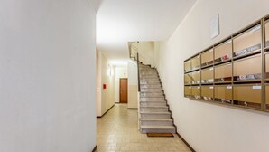 A hallway with a staircase, a fire alarm, and a wall with storage boxes. - GuestHost - Functional and modern studio apartment of approximately 17 sqm located on the ground floor of a renovated period building WITHOUT a lift (one step to access it). The apartment is located in a quiet, traffic-free street, just a 7-minute walk f (Padova)