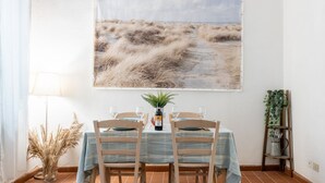 Un comedor con una mesa preparada para dos personas, un cuadro en la pared y una planta a un lado.