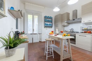 Una cocina con armarios blancos, encimera de madera, una planta colgante y una mesa con taburetes.