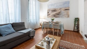 Una sala de estar con sofá, una mesa de comedor con sillas, una mesa de centro y un cuadro en la pared.