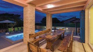 An outdoor patio with a pool, wooden benches, and a stone pillar. - Villa with swimming pool, terrace and barbecue (Peroj)