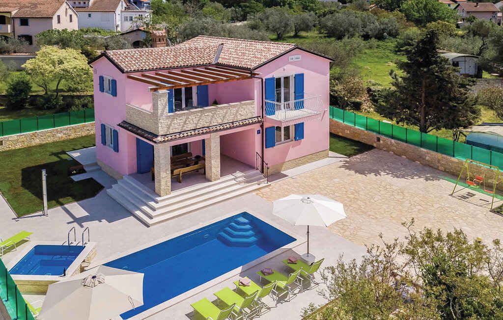 Una casa rosa a due piani con un balcone, una piscina e un'area salotto esterna.