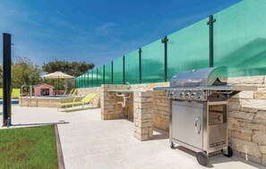 An outdoor patio with a stone barbecue grill and a sink, surrounded by a green fence. - Villa with swimming pool, terrace and barbecue (Peroj)