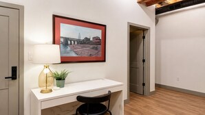 A room with a desk, chair, lamp, potted plant, and a framed picture on the wall.