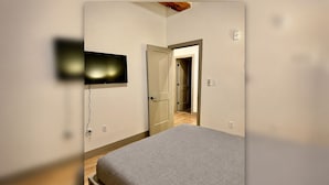 A bedroom with a bed, a TV mounted on the wall, and a door leading to another room.