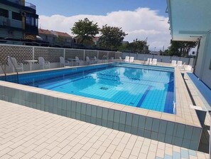 Ein rechteckiger Pool mit Fliesenränder, umgeben von einer gefliesten Liegefläche.
