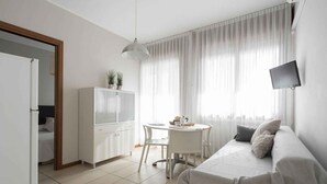 Una habitación moderna y luminosa con sofá, mesa de comedor y televisión montada en la pared.