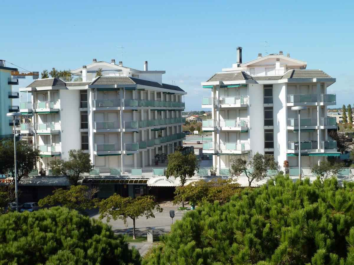 A multi-story residential building with balconies, a parking area, and surrounding greenery.