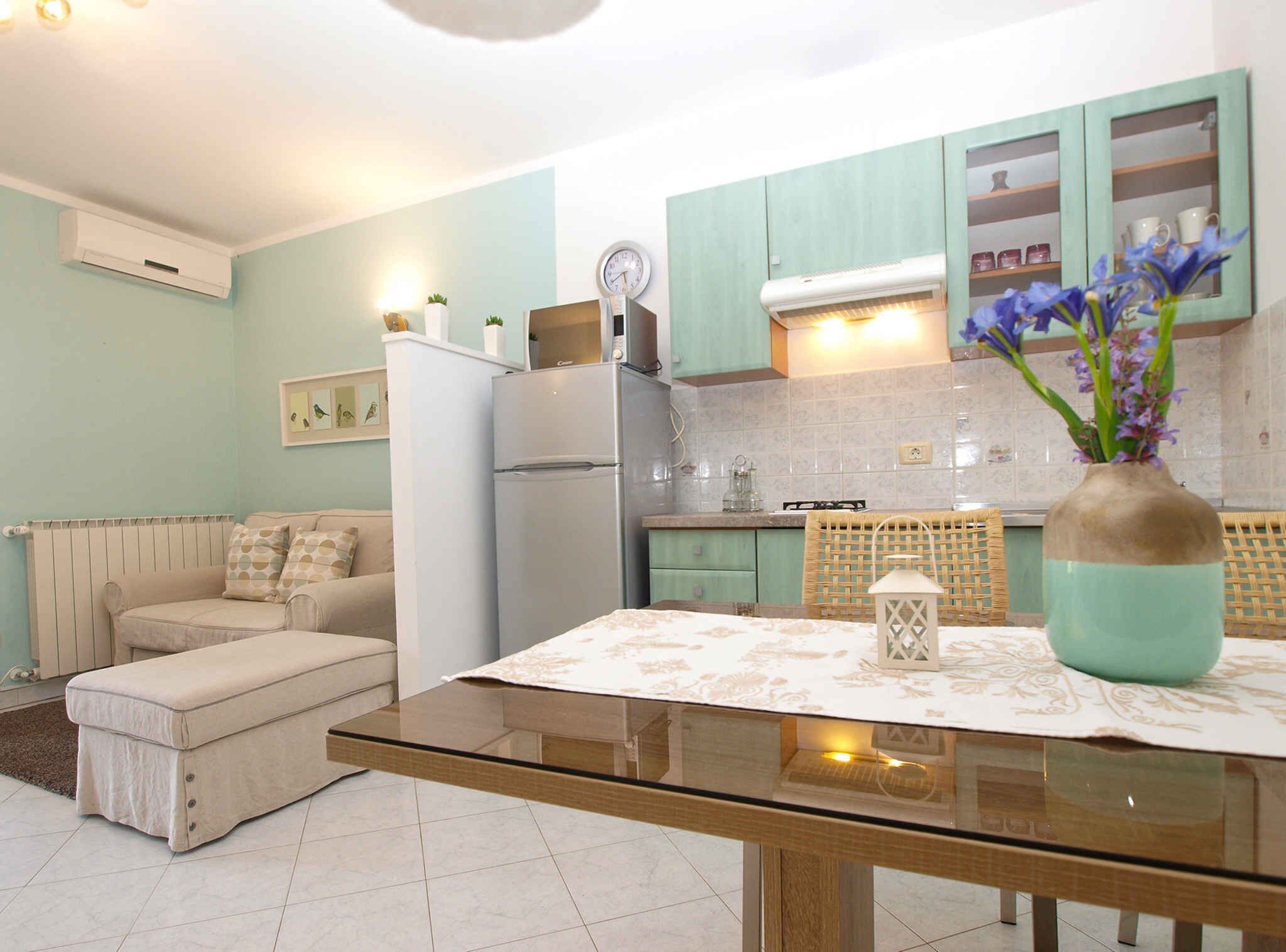 Een moderne keuken met blauwgroene kastjes, een witte koelkast en een eethoek met een glazen tafel.