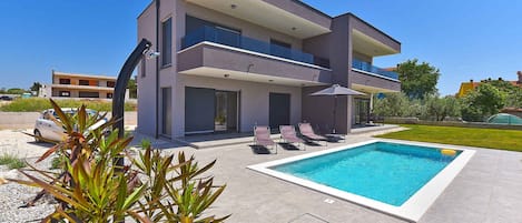 Et moderne hus med to etager, en swimmingpool, udendørs siddepladser og en velplejet have.