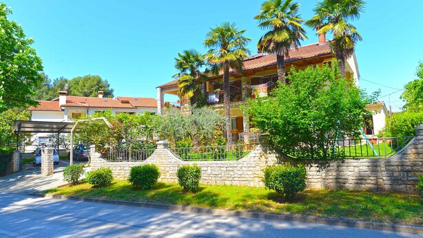 A two-story house with a stone wall and a covered driveway. - Holiday apartment with air conditioning (Poreč)
