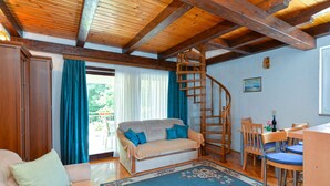 A cozy living room with a sofa, a coffee table, a dining area with chairs, a spiral staircase, and a large window with curtains. - Holiday apartment with air conditioning (Poreč)
