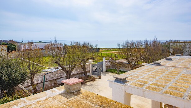 A rooftop terrace with a view of the sea, stone walls, and a garden area.