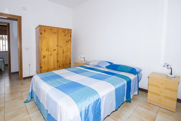 A bedroom with a bed, wooden wardrobe, bedside table, and a lamp.
