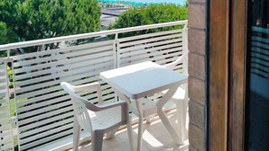 Un balcón con mesa y sillas, con vistas a una zona costera con vegetación y una torre distante.