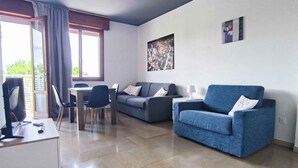 Una sala de estar moderna con un sillón azul, sofá gris y un comedor con una mesa y sillas.