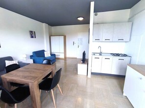 A modern apartment with a dining area, a blue sofa, a kitchen with white cabinets, and a wooden dining table.