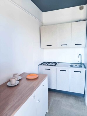 A compact kitchen with a wooden countertop, a gas stove, a sink, and white cabinets.