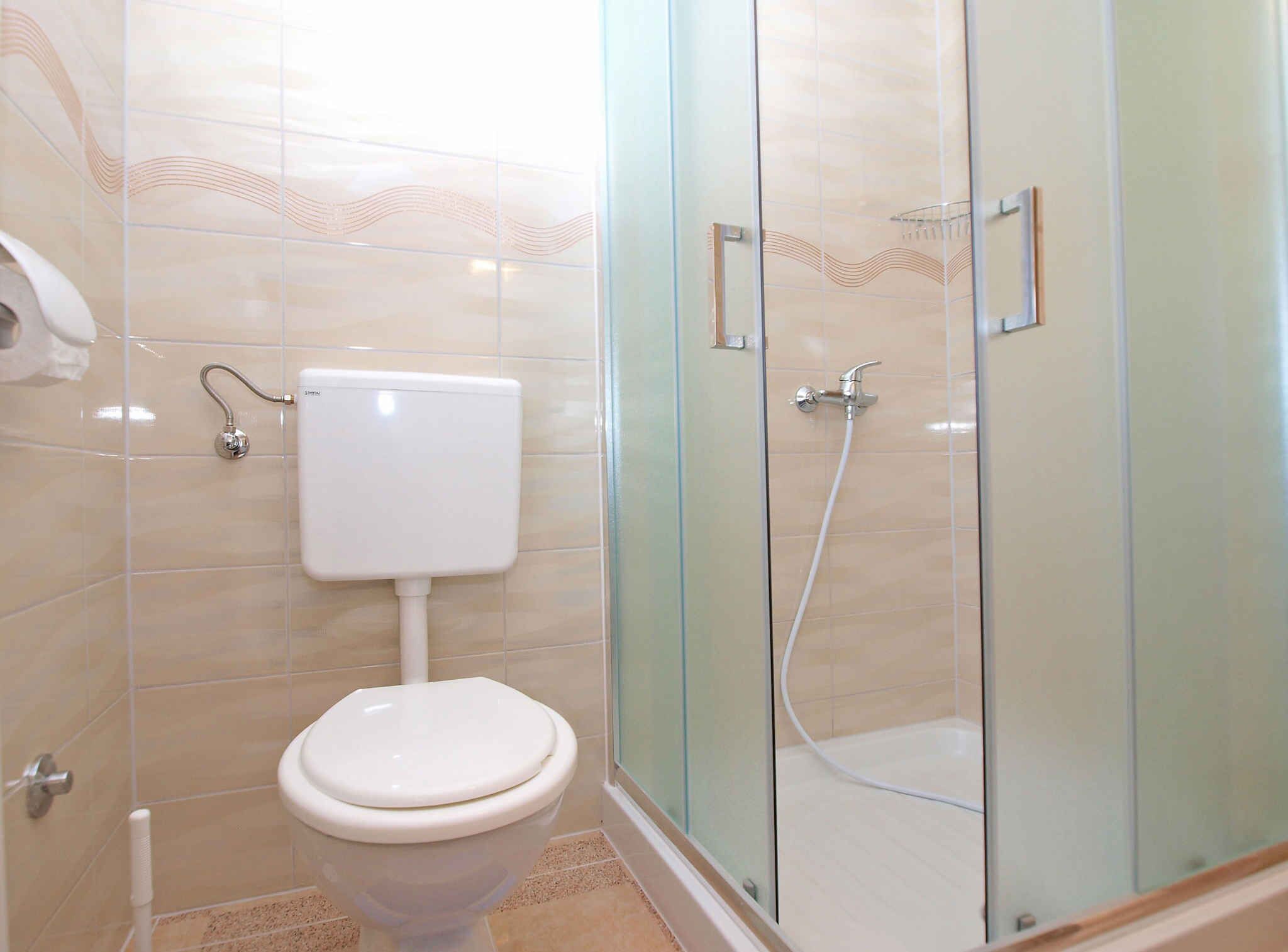 Une salle de bain comprenant des toilettes, une douche à parois de verre et des murs carrelés.