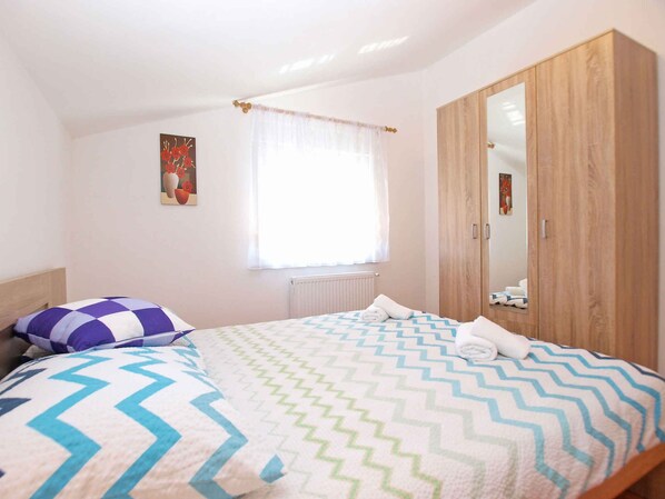 A bedroom with a bed, a wardrobe, a window with curtains, and a painting on the wall.