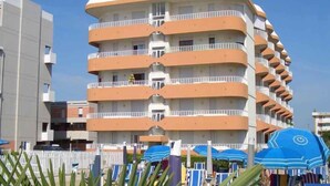 A multi-story hotel with balconies, a white and orange facade, and beach umbrellas in the foreground. - Holiday apartment with balcony and air conditioning (Lido di Jesolo)