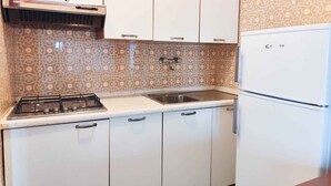 A kitchen with a gas stove, sink, white cabinets, patterned backsplash, and a white refrigerator. - Holiday apartment with balcony and air conditioning (Lido di Jesolo)