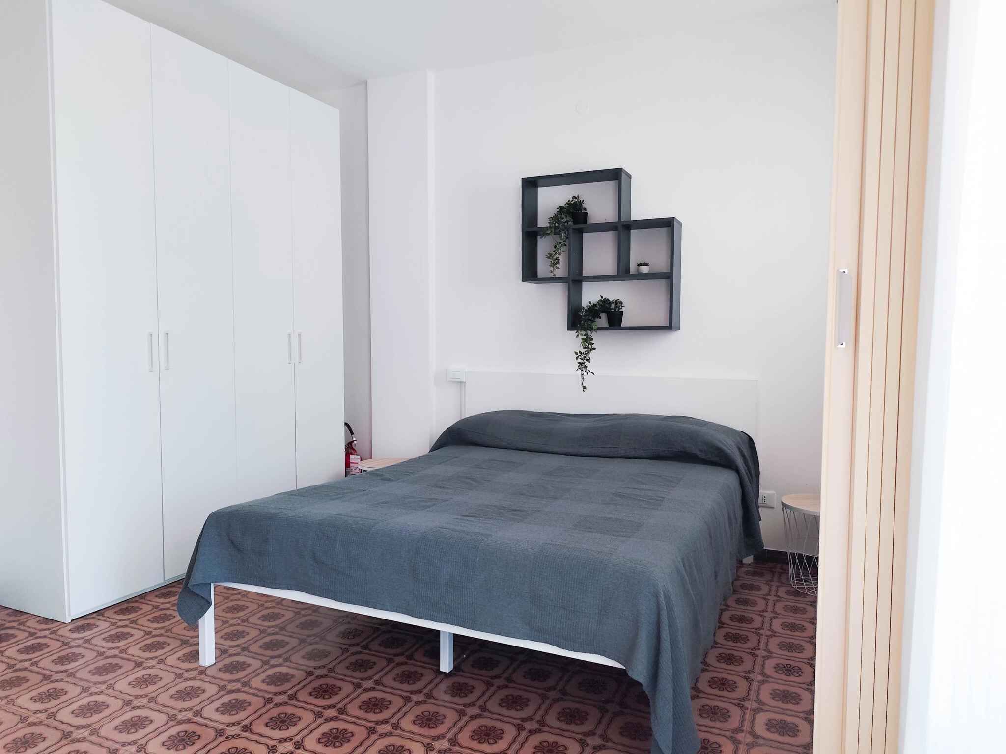 A bedroom with a bed, a wardrobe, and a wall-mounted shelf with plants.