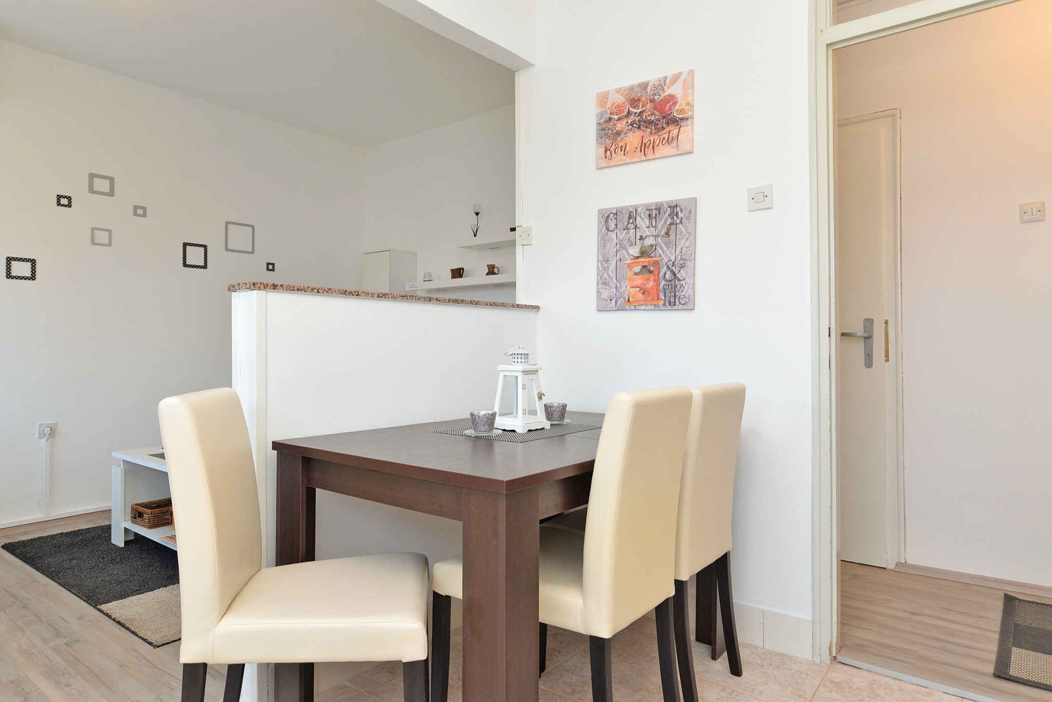 A dining area with a wooden table and four chairs, a small white cabinet, and a wall-mounted shelf with decorative items.