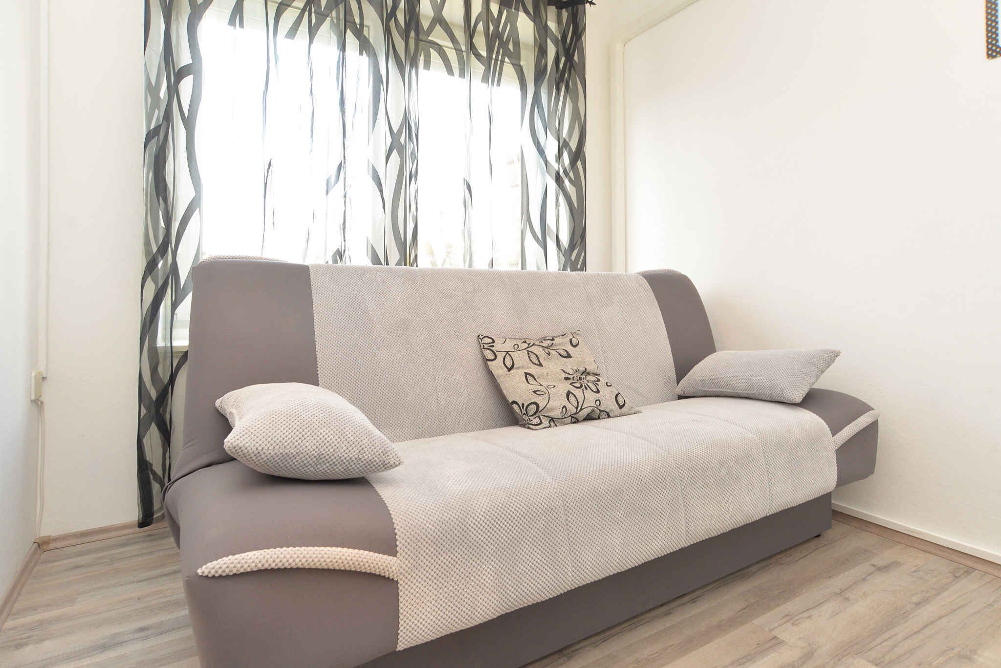 En moderne sofa i neutrale farver, placeret foran et vindue med lette gardiner.